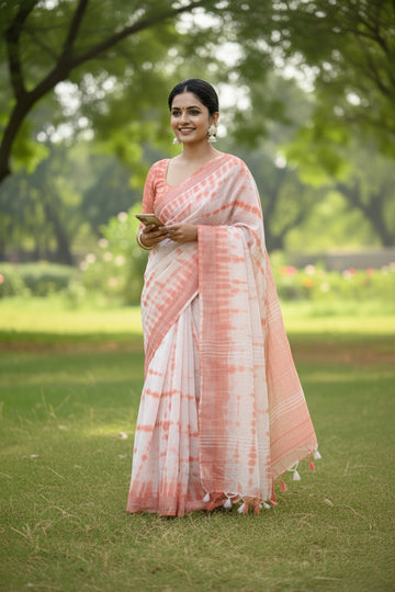 Woman in a pink and white saree sitting on grass with a blurred green background